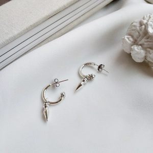 Macro detail of silver drop earrings with cone pendants on textured white fabric