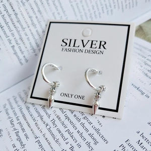 Detailed macro view of silver dagger pendant earring on a white jewelry card with book background