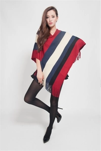 Detail of red and blue striped knitted poncho featuring decorative tassel fringe hem