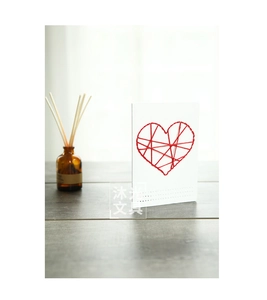 Close-up of white greeting card with handcrafted red stitched heart on a wood table