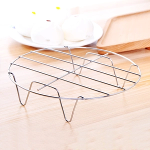 Stainless steel round steaming rack with four legs on a minimalist wooden kitchen table