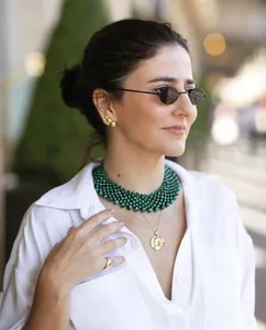 Detail of vintage oval sunglasses and layered green beaded necklaces with gold accents
