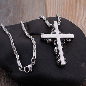 Polished stainless steel cross pendant with skull motif on a rustic wood and stone background