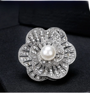Detailed close-up of a silver flower brooch with white pearls and sparkling rhinestones