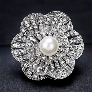 Elegant silver flower brooch with sparkling rhinestones and white pearl center on black background