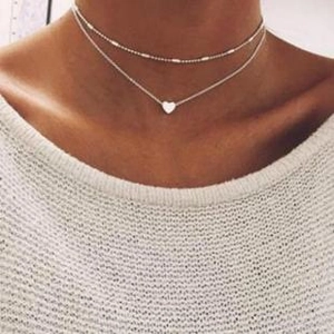Detail view of silver double-layered necklace with bead bar and heart pendant on model