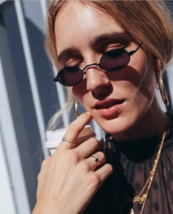 Close-up of retro black oval sunglasses with gold necklaces on model in sunlight