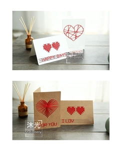 Close-up of DIY cross-stitch heart greeting card with red thread on kraft paper