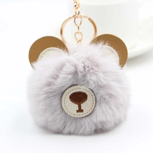 Close-up of a fluffy grey faux fur bear keychain with brown leather ears and golden metal ring