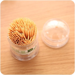 Bamboo toothpicks in a transparent portable dispenser on a wooden table surface