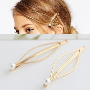 Detailed view of hollow fish-shaped golden hair clip with pearl accent on model