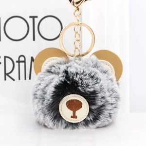 Close-up of a fluffy plush bear keychain with grey faux fur and a golden metal ring