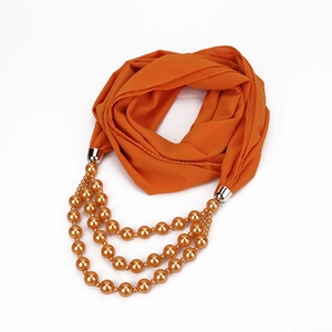 Detail eines orangefarbenen Chiffonschals mit mehrlagiger Goldperlenkette und Metallteilen