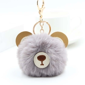 Detail of cute grey faux fur pompom keychain with brown leather bear ears and gold metal clasp