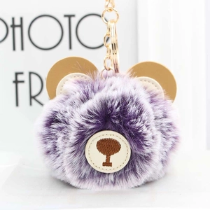 Macro detail of purple plush bear keychain with faux fur ball and gold metal clasp