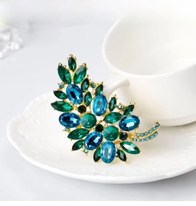 Macro shot of elegant leaf brooch with blue and green crystals on a porcelain cup edge