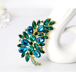 Detailed view of leaf brooch with emerald and sapphire crystals on gold-tone base