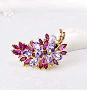 Detailed close-up of a floral brooch with purple and magenta crystals on a gold base