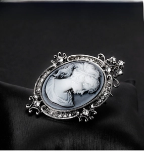 Macro shot of vintage cameo brooch with silver rhinestone frame on black silk background
