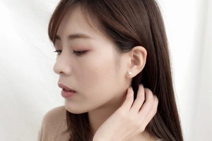 Close-up of elegant cat ear pearl stud earrings worn by a model on white background