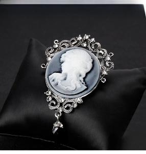Detailed close-up of a vintage oval cameo brooch with crystal accents and black teardrop pendant