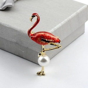 Detailed close-up of a red flamingo brooch with gold trim and white pearl on a gift box