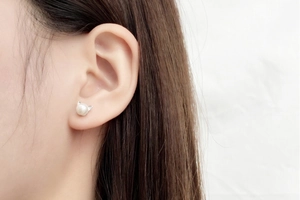 Detailed view of a cute pearl earring with silver cat ear accent worn on a model's ear