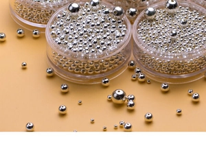 Macro shot of assorted silver metal beads in various sizes on a bright yellow surface