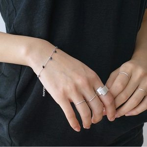 Close-up of minimalist brushed silver rings and a beaded chain bracelet on model hand