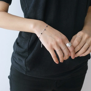 Close-up of minimalist brushed silver rings and beaded chain bracelet on model hand