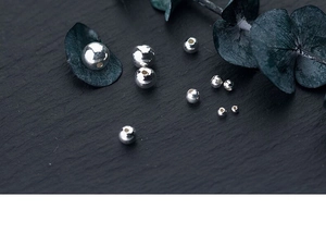 Macro detail of various sized polished silver round beads on a dark textured stone