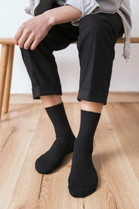 Close-up of black ribbed cotton mid-calf sock on person with minimalist home background