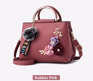 Detail of pink embroidered handbag with floral charms and a fuzzy pom-pom accessory
