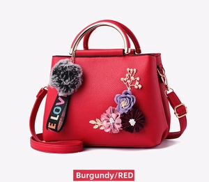 Detail of burgundy leather handbag with 3D floral accents and plush pompom charm