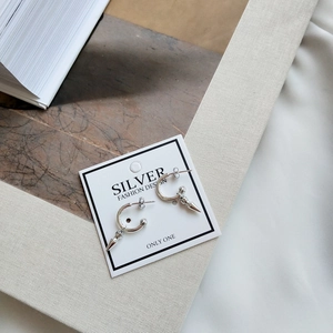 Silver hoop earrings with spike pendants on a minimalist branded card presentation