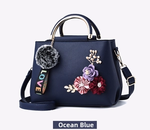 Detail of blue textured leather handbag with 3D floral accents and gold metal handles