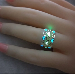 Glow-in-the-dark hollow heart ring with blue and green luminescence on model's hand