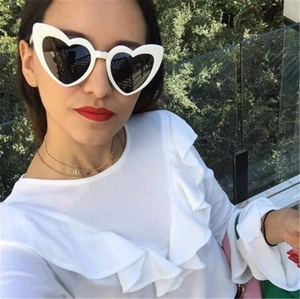 Close-up of white heart-shaped sunglasses with dark lenses worn by a model outdoors