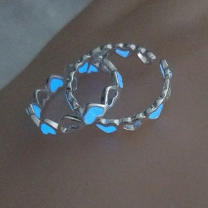 Close-up of two silver hollow heart rings featuring a vibrant blue luminous glow in the dark