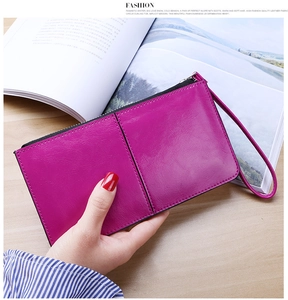 Detailed view of rose red leather wristlet with black zipper on a wooden desk