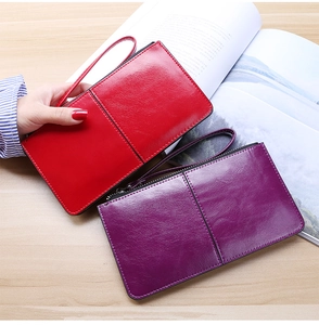 Detail view of red and purple long leather clutch wallets with wristlet on wooden table