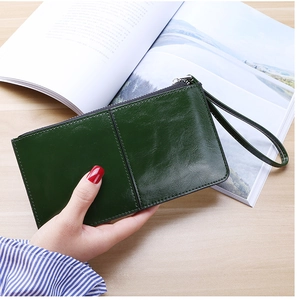 Close-up of a dark green leather long wallet with wrist strap on a wooden desk