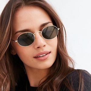 Close-up of golden oval metal sunglasses with dark lenses on female model
