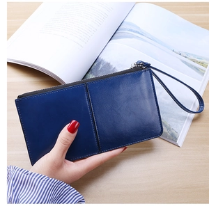 Blue leather long wallet for women with wristlet strap held against a magazine