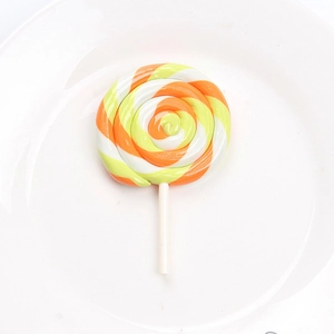 Macro shot of an orange and yellow swirl clay lollipop accessory on a white plate