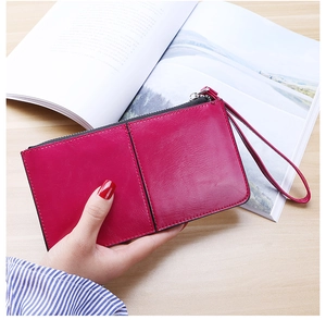 Close-up of rose red leather clutch wallet with wristlet strap held against a magazine