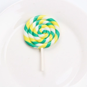 Top view of a large green and yellow swirl clay lollipop on a white ceramic plate