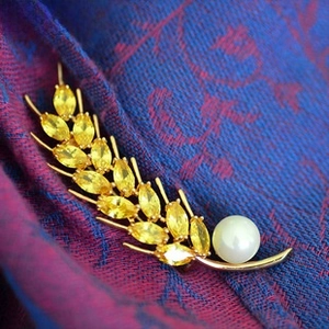 Macro detail of wheat ear brooch with gold base, yellow rhinestones and white pearl