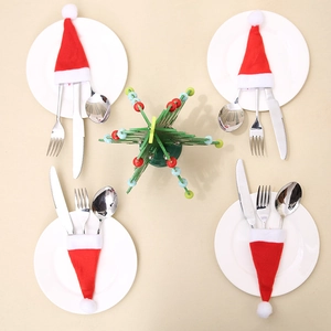 Four sets of red and white Santa hat cutlery holders arranged on a festive wooden table