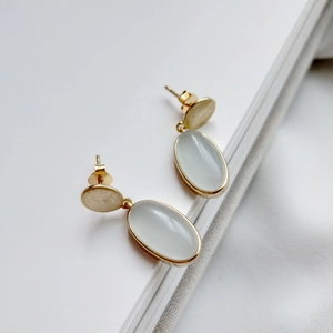 Detailed close-up of 925 silver stud earrings featuring light blue stones and golden finish